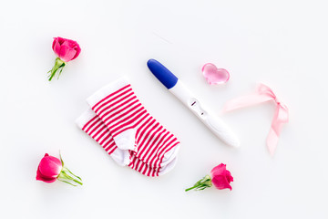 Pregnancy and preparation for childbirth. Babyshower. Pregnancy test near socks and flowers white background top view