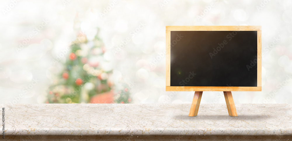 Poster blackboard on White marble table top at blur bokeh christmas tree decor with string light background when show falling,Winter holiday greeting card
