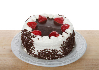 Chocolate cake frosting in vanilla cream with chocolate glaze topping surrounded by fresh cut strawberries dipped in glaze. Chocolate chip morsels pressed into the side of cake. Isolated.