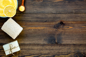 Lemon spa salt and spa assessories like soap, loofah, spa oil on dark wooden background top view space for text