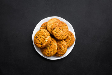 Homemade oatmeal cookies on white plate on black background top view copy space