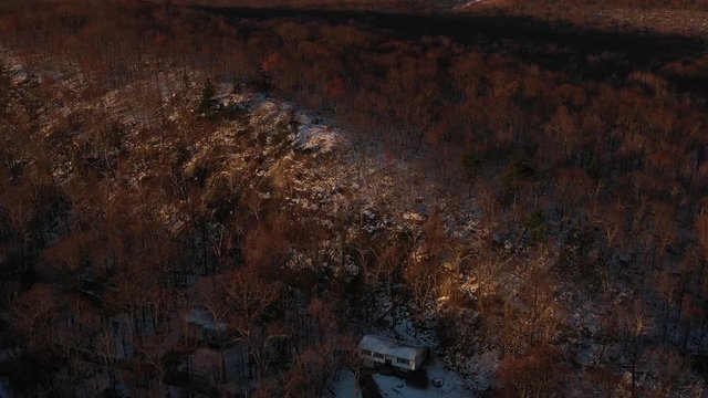 Drone fly to snowy ridge forest at sunrise.  A small house in view.  in 4K.