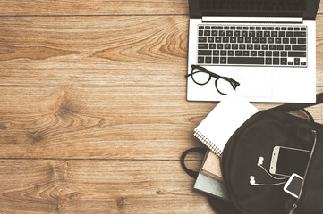 Laptop, backpack, books, notebook, phone, headphones and glasses on wooden background. Top view