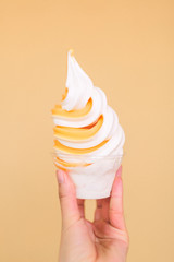 A hand holding an orange ice cream dessert agains an orange wall. 