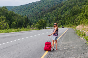 a young woman walking on the highway with a suitcase in the summer. A woman and a suitcase