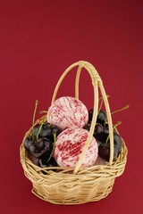 Cherry Bath Bomb. striped bombs for a bath set and ripe sweet cherry berries in a wicker basket on a bright burgundy background. Organic cosmetics with sweet cherry extract