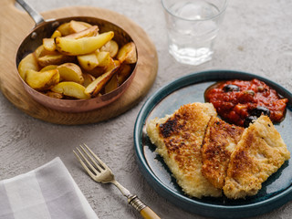 Fried fish with tomato-olive sauce and potatoes.