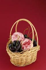 Fototapeta na wymiar Cherry Bath Bomb.Pink striped bombs for a bath set and ripe sweet cherry berries in a wicker basket on a bright burgundy background. Organic cosmetics with sweet cherry extract