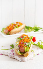 Hot dog with  cucumber, carrot, tomato and lettuce on wooden background. Fast food menu.