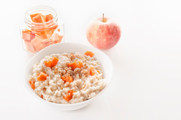 Oatmeal with pumpkin and nuts in a plate, an apple and sliced carrots on a white background. Close-up. Copy space