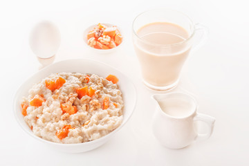 Fototapeta na wymiar Oatmeal with pumpkin and nuts in a plate, a glass of tea, a boiled egg and a jug with milk on a white background. Close-up.
