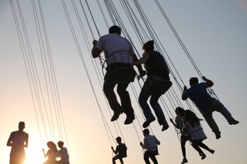 Silhouette of young people on Ferris wheel and swinging carousel in stop motion on sunset background