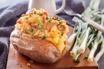 Baked potatoes with bacon, mushrooms and green onions in a rustic style on a wooden board. Close-up