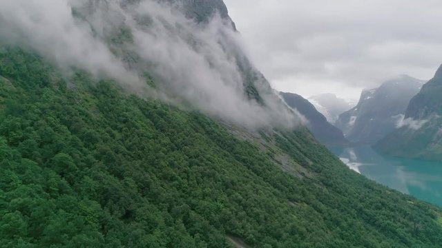 Epic drone shot with spooky fog floating on the mountainside, with a blue lake and gletsjer on the background