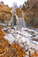 Partially frozen waterfall with leaves on ground