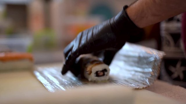 Male hands in black rubber gloves are making sushi rolls . Preparing sushi set for the client. Blurred background