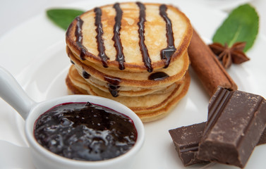 Pancakes with jam and chocolate, on a white plate decorated with fresh mint