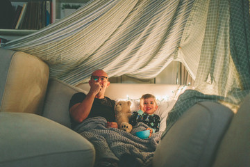 Fototapeta A father and son watching a movie in a fort and eating popcorn.  obraz