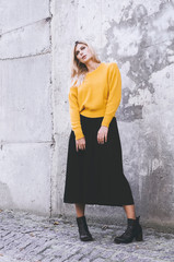 Fashionable girl. A girl in a yellow sweater, wearing a black skirt and boots in the background of a concrete wall. Clothes in style oversize