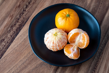 Black plate of satsuma oranges on a rustic wood table, two oranges peeled, one sectioned