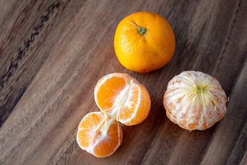 Three satsuma oranges on a rustic wood table, two oranges peeled, one sectioned