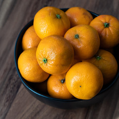 Black bowl of satsuma oranges on a rustic wood table