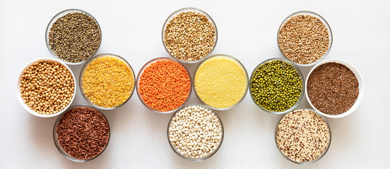 Flat lay set of glass bowls with healthy cereals, beans and seeds on white background.
