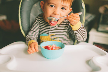 A toddler eating cereal in a highchair. 