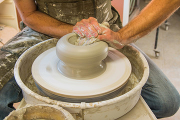     Artist potter in the workshop creating a jug out of earthenware, hands closeup. Twisted potter's wheel. Small aristic craftsmen business concept. 