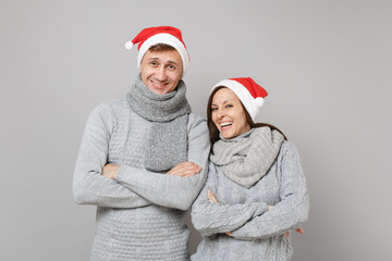 Merry fun couple girl guy in red Santa Christmas hat gray sweaters scarves isolated on grey wall background, studio portrait. Happy New Year 2019 celebration holiday party concept. Mock up copy space.