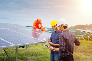 Engineers and workers in uniform and installs solid solar panels on a metal base in a solar farm.