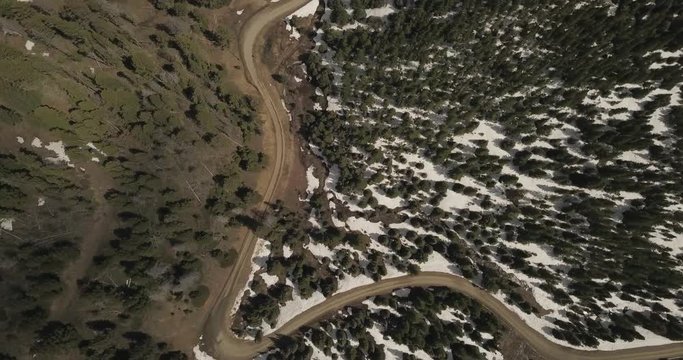 Beautiful narrow road between two forests, with green spruce trees at the start of summer season with snow melting on Beartrap trail
(drone shot)