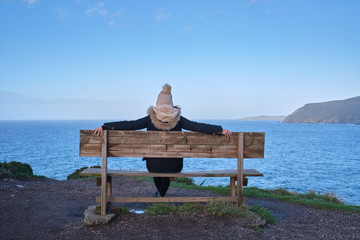 Una chica mira el mar sentada desde un banco