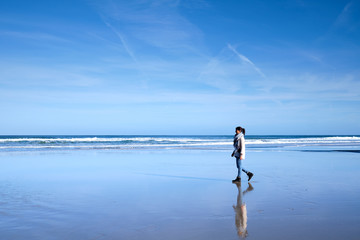 Una chica joven pasea por la costa de una playa donde se refleja el cielo