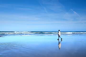 Fototapeta na wymiar Una chica joven pasea por la costa de una playa donde se refleja el cielo