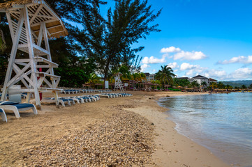 Jamaica Beach. Sun chairs by the palm trees and sea by the calm sea in Montego Bay, Jamaica. Beautiful sky and clouds.