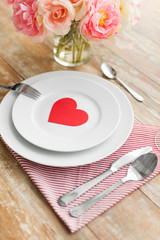 valentines day, table setting and romantic dinner concept - close up of plates with cutlery, flowers in vase and napkin