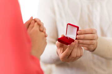 valentines day, proposal and engagement concept - man giving diamond ring in little red gift box to...