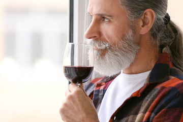 Senior man drinking wine near window at home