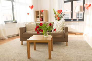 valentines day, holidays and interior concept - red flowers on table in living room or home decorated with heart shaped balloons