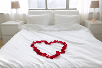 valentines day, romantic date and holidays concept - bed decorated with heart made of red petals in bedroom at home