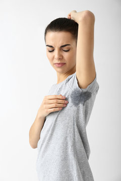 Young woman with wet spot on clothes under armpit against white background. Concept of using deodorant