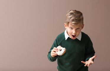 Angry little boy with donut on color background