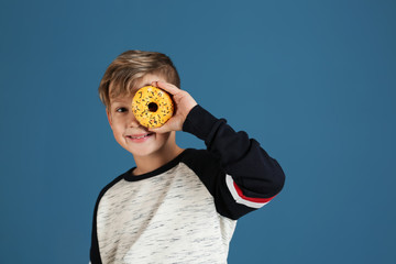 Cute little boy with donut on color background