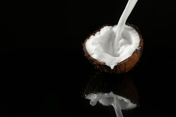 Half of ripe coconut and splash of milk on dark background