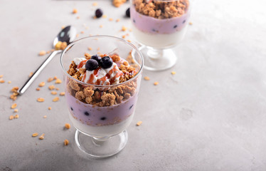 Tasty granola with yogurt in glass on grey table