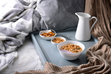 Bowls with tasty granola and yogurt on bed