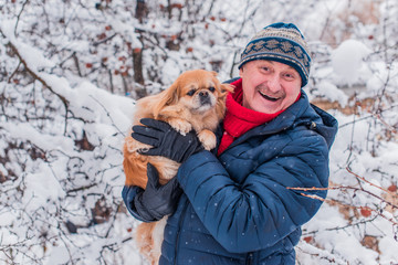 Senior man dog lover with his red pekingese pet on a walk at snowy park. Concept love and care of animals. Good people caring for pets