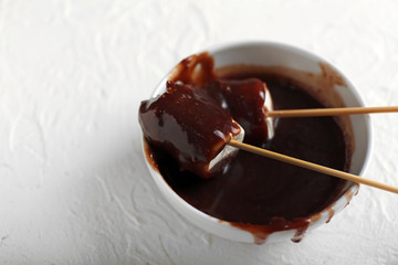 Tasty marshmallows dipped into melted chocolate on white textured background
