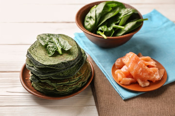 Tasty green pancakes with spinach and salmon on wooden table